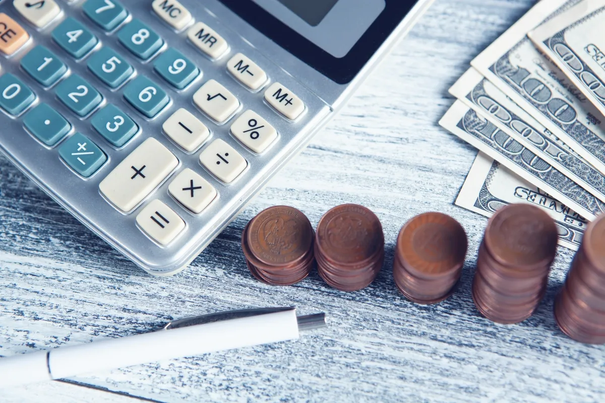 Calculadora, caneta e dinheiro sobre uma mesa